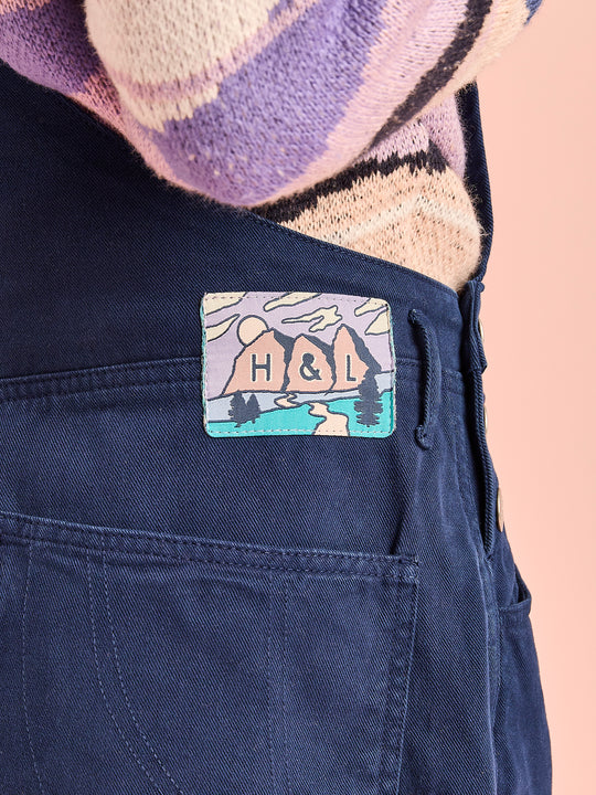 Detail shot of the branded mountain inspired badge on the waistband of the functional dungarees