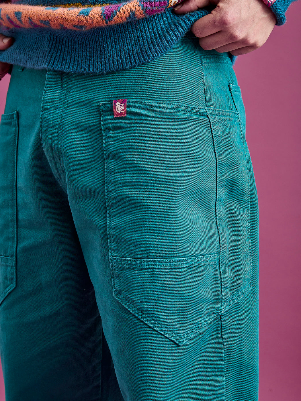 Detailed shot of the front pocket featuring seams and the branded badge on the teal trousers
