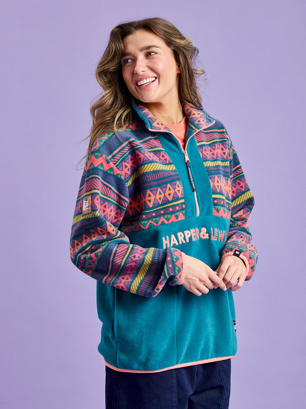 Female Model wearing an aztec & teal fleece with details such as a badge on the sleeve and embroidered 'Harper & Lewis' logo.